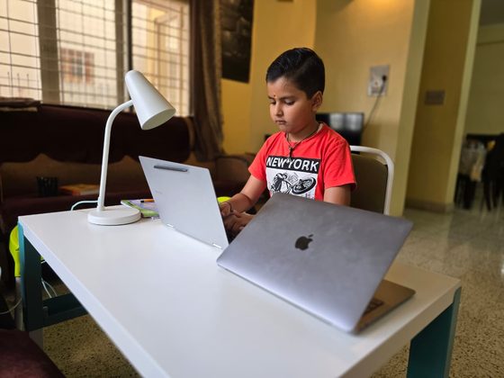 Vrishvardhan Sharma working at a desk with two laptops and a reading lamp.