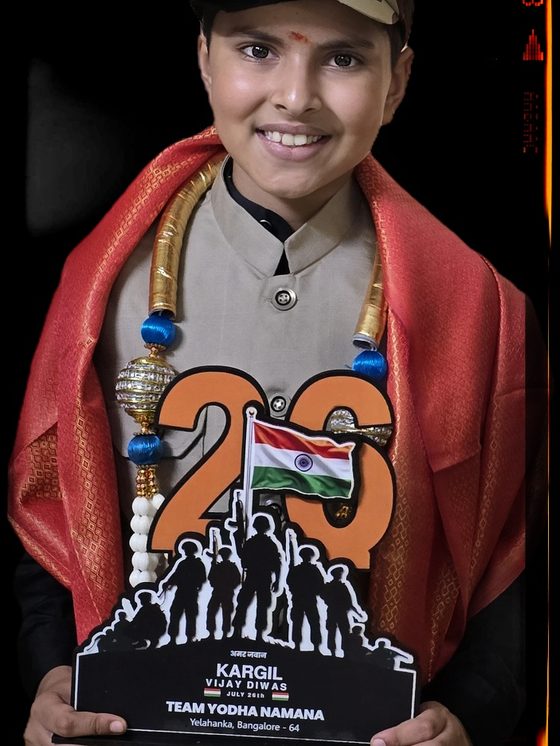 Vrishvardhan Sharma in an army cap and shawl holding a Kargil Vijay Diwas trophy shaped like a mountain ridge.