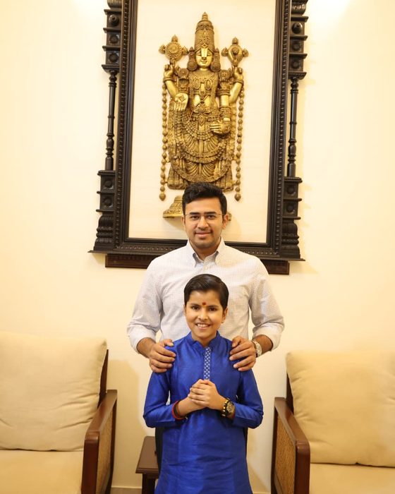 Shri Tejasvi Surya standing behind Vrishvardhan Sharma with his hands on his shoulders, beneath a brass Venkateshwara relief.