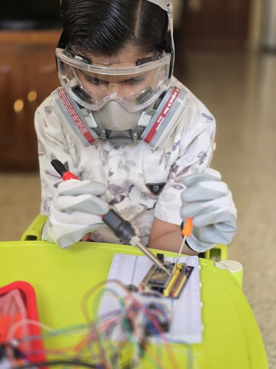 Vrishvardhan Sharma soldering a breadboard circuit, wearing safety goggles and a respirator.