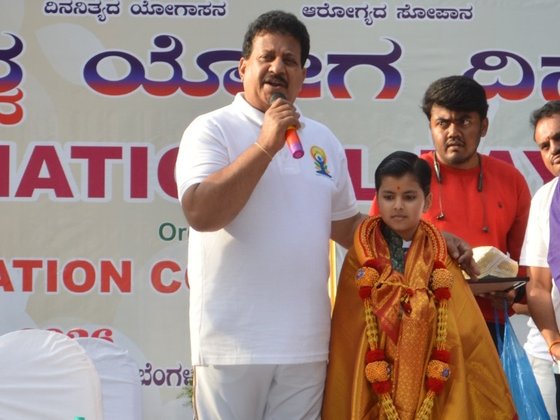 Shri S. R. Vishwanath speaking on stage beside Vrishvardhan Sharma at the International Yoga Day event, Yelahanka, Bengaluru.